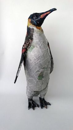 a penguin made out of newspaper sitting on top of a white surface with its head turned to the side