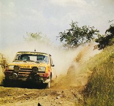 a car driving down a dirt road with trees in the backgrouund and dust flying around