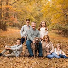 a family posing for a photo in the woods with their dog and two children, all dressed in fall colors