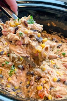 a hand holding a spoon full of chicken and corn casserole in a crock pot