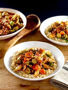 two bowls filled with chicken and veggies on top of rice next to a wooden spoon