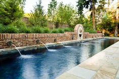 an outdoor swimming pool surrounded by brick walls and water features, with two fountains running from the side