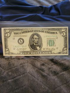 a one dollar bill in a clear plastic case on a bed with a blue blanket