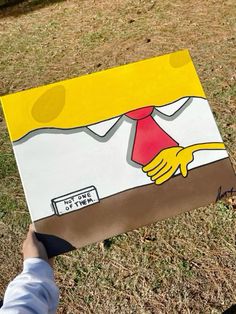 a person holding up a cardboard box with a painting on it's side in the grass