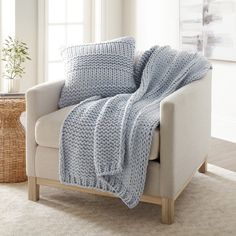 a white chair with a blue blanket on top of it next to a wicker basket