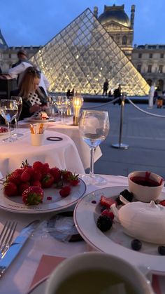 two plates with strawberries on them are sitting next to wine glasses and desserts