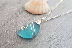 a blue sea glass pendant on a silver chain next to a seashell and shell