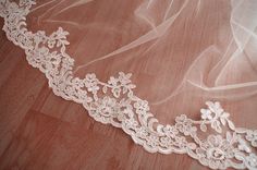 a wedding veil with flowers on it laying on a wooden floor next to a pair of scissors