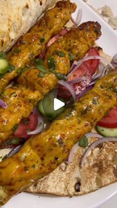 a white plate topped with meat covered in sauce and veggies next to pita bread