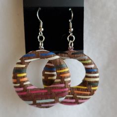 two pairs of wooden earrings with multicolored strips hanging from hooks on a white background