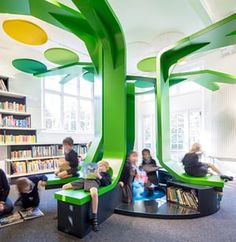 children are sitting on benches in the library with bookshelves and trees painted green