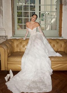 a woman in a white wedding dress standing on a couch with her arms around her body