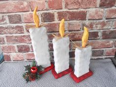 three white candles are sitting next to each other on a table near a brick wall