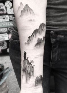 a person with a tattoo on their arm that has mountains and trees in the background