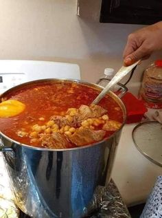 a person is cooking food in a large pot on the stove top with a ladle