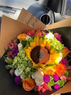 a bouquet of flowers sits in the front seat of a car with a note attached to it