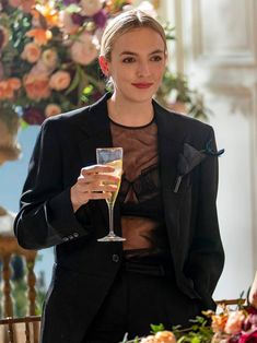 a woman is holding a wine glass in her hand while sitting at a table with flowers