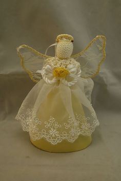 a small yellow angel sitting on top of a white table cloth covered jar filled with flowers