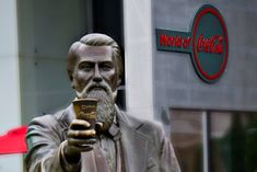 a statue of a man holding a cup in front of a coca - cola sign