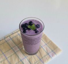 a smoothie with blueberries and mint is on a yellow cloth next to a napkin