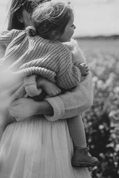 a black and white photo of a woman holding a baby in her arms while standing in a field