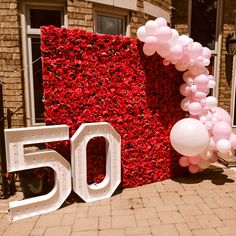 a sign that says 50 with balloons on it and a bunch of flowers behind it