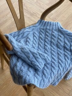 a blue knitted blanket sitting on top of a wooden chair next to a wood floor