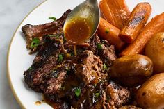 a white plate topped with meat, potatoes and carrots next to a spoon filled with gravy