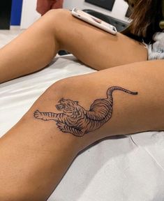 a woman laying in bed with a tiger tattoo on her arm and leg, next to a cell phone