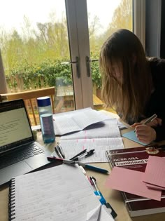 a woman sitting at a table with papers and pens in front of her laptop computer