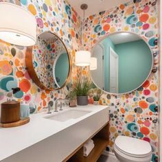 a bathroom with colorful wallpaper and two round mirrors