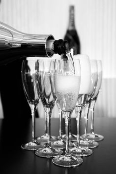 several wine glasses are lined up on a table with a bottle being poured into them