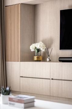 a vase with white flowers sitting on top of a wooden shelf in front of a flat screen tv