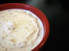 a red bowl filled with white sauce sitting on top of a black table next to a knife