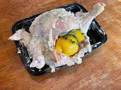 a chicken with lemons and herbs on it in a plastic container sitting on a wooden table