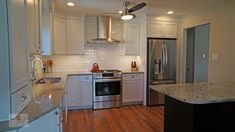 a kitchen with white cabinets and stainless steel appliances in the center, along with hardwood floors