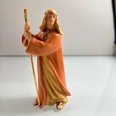 a figurine of jesus holding a staff and wearing an orange robe with gold trim