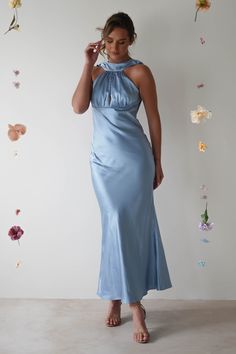 a woman in a long blue dress standing next to a wall with flowers on it