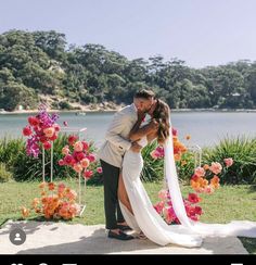 a bride and groom kissing in front of flowers at their wedding ceremony by the water