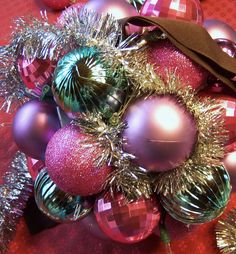 a bunch of shiny christmas ornaments on a red tablecloth with silver tinsels