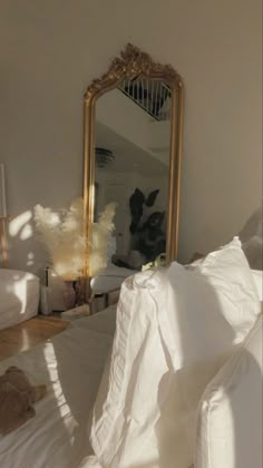 a bed with white sheets and a gold framed mirror