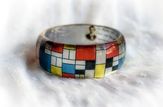 Mondrian Resin Bangle, Famous Art Jewelry, Resin Bracelet Mondrian Born 7 March 1872 - Died 1 February 1944 (aged 71) Middle design thick bangle - Height of the bangle - 3cm/1.18inches Pieter Cornelis Mondrian was a famous abstract Cubism painter, born in the Netherlands. His most recognized works are abstract paintings of colored squares, rectangles, and thick black lines.We love his minimal art , and that's why we decided to create a bracelet with his design in red, yellow, white and blue squa Multicolor Wearable Art Bangle Bracelets, Multicolor Bangle Bracelets In Wearable Art Style, Multicolor Wearable Art Bracelet For Gift, Artistic Multicolor Bangle Bracelet, Artistic Multicolor Cuff Bracelet As A Gift, Artistic Multicolor Cuff Bracelet Gift, Artistic Multicolor Cuff Bracelet As Gift, Artistic Handmade Bangle Bracelets, Abstract Cubism