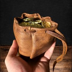 a hand holding a brown leather pouch with gold coins in it