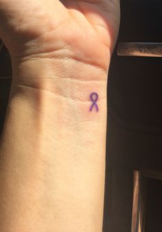 a person with a small tattoo on their wrist that has a purple ribbon on it