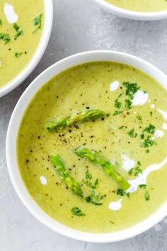 three bowls filled with broccoli soup on top of a white table next to silver spoons