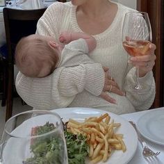 a woman holding a baby in her arms while sitting at a table with food and wine glasses