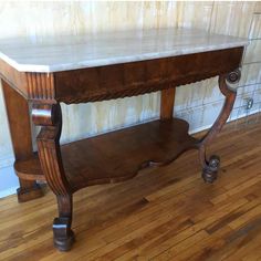 an old wooden table with marble top on hardwood floor next to tile wall and wood flooring