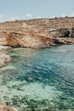 the water is crystal blue and clear at this rocky beach area with people swimming in it