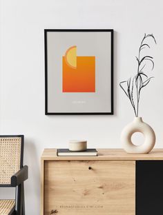 a white vase sitting on top of a wooden dresser next to a framed art piece