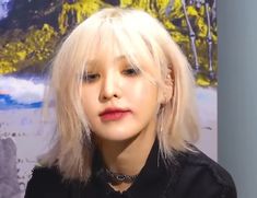 a woman with blonde hair and black shirt in front of a painting on the wall